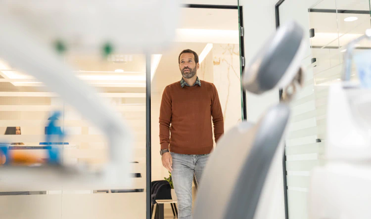 Desktop_Home_Convenient_Wall_Township_Location A man in a brown sweater and jeans walks into a modern, brightly lit dental office, with dental equipment visible in the foreground.