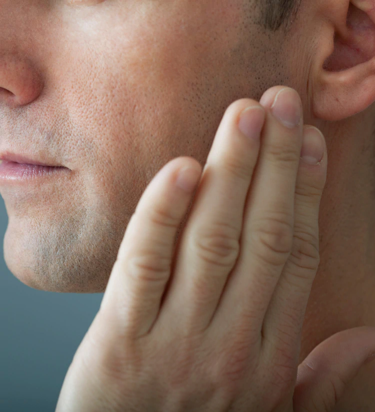 A close-up of a person touching their jawline with their fingers, focusing on the side of their face and ear.