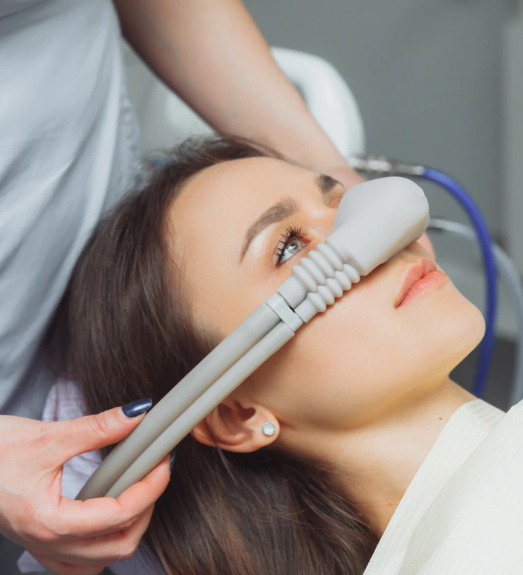 A woman lies back while a healthcare professional places a nitrous oxide (laughing gas) mask over her nose, likely preparing her for a dental or medical procedure.