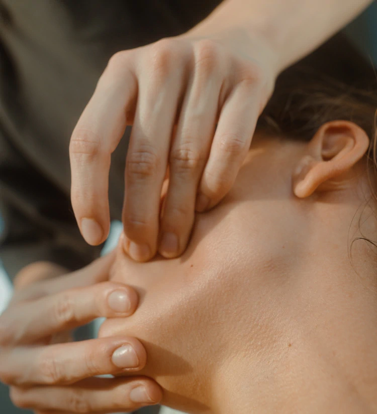 Close-up of a person receiving a facial massage, with another persons hands gently pressing on their cheek and jawline.