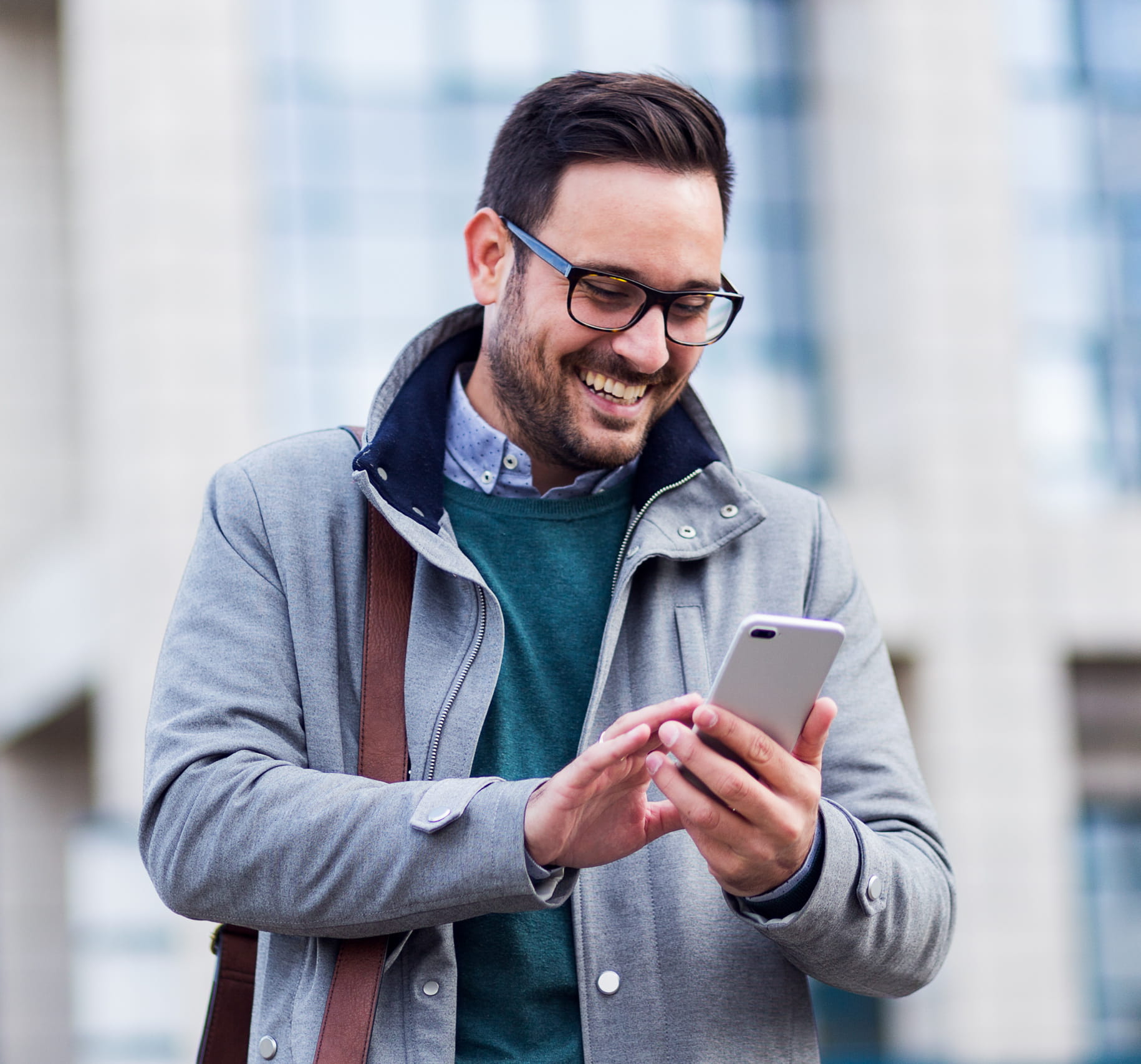 ReGenCare2_AdobeStock_228679121_1_cropped Recovery-focused care for Oral & Maxillofacial Surgery in Wall Township NJ A smiling man in a coat and glasses looks down at his smartphone while standing in front of a modern office building.